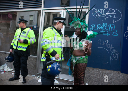 Eine schwarze weibliche Karneval Performer gekleidet in grünen Gespräche an einem weißen Polizisten in Kampfmontur in Portobello Road. Stockfoto
