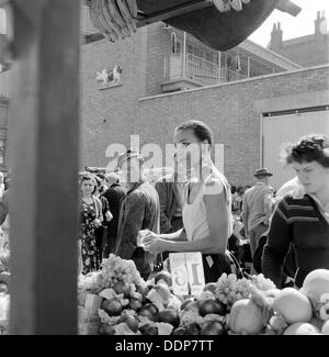 Eine Frau kauft Obst in einem Stall in einem Markt, North London Street, c1946-c1959. Künstler: John Gay Stockfoto