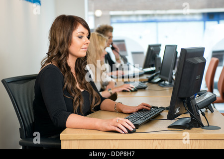 Junge männliche und weibliche Büroangestellte beantworten Telefone & arbeiten mit Computern in einer modernen Büroumgebung Stockfoto