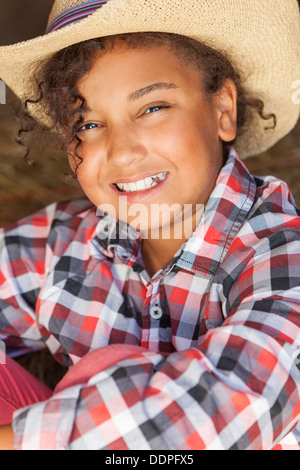 Schöne, glückliche Mischlinge African American female Mädchen Kind trägt Cowboy Strohhut & kariertes Hemd sitzt im Heu gefüllten Scheune Stockfoto