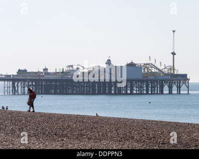 Mann zu Fuß auf Brighton Beach mit einem Metalldetektor mit Palace Pier im Hintergrund Stockfoto