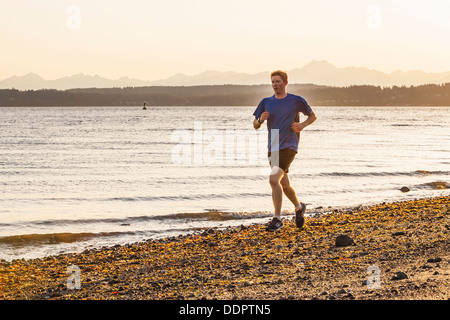 Ein junger Mann an einem Strand in Seattles Entdeckerpark ausgeführt. Seattle, Washington, USA. Stockfoto