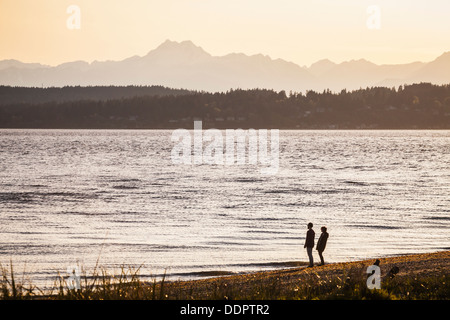 Ein Mann und eine Frau stehen am Strand, Blick auf den Puget Sound und die Olympic Mountains im Discovery Park in Seattle Wa Stockfoto