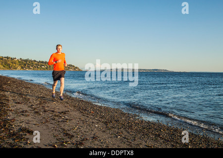 Ein junger Mann läuft an einem Strand in Discovery Park, Seattle, Washington, USA. Stockfoto