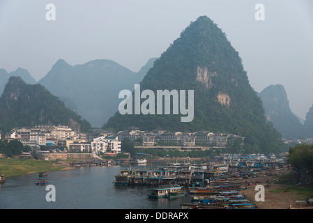 Ausflugsboote in den Li-Fluss mit einer Stadt am Wasser, Yangshuo, Guilin, Provinz Guangxi, China Stockfoto