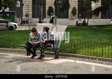 Zwei Mädchen im Teenageralter ruhen auf einer Parkbank in Piazza Bra, Verona, mit Postern von ihren Liebsten eine Richtung Bandmitglieder. Stockfoto