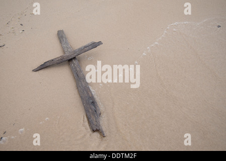 Kreuz gemacht, Treibholz, liegend im Sand mit einer Welle über sie waschen Stockfoto