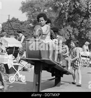 Kinder, die auf einem Schaukelpferd, clissold Park, Stoke Newington, London, 1962-1964. Schöpfer: John Gay. Stockfoto