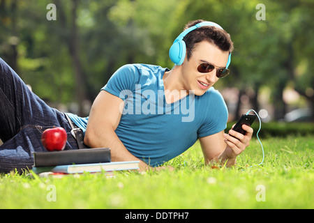 Gut aussehend männlichen Studenten auf einer Wiese liegen und Musik hören Stockfoto