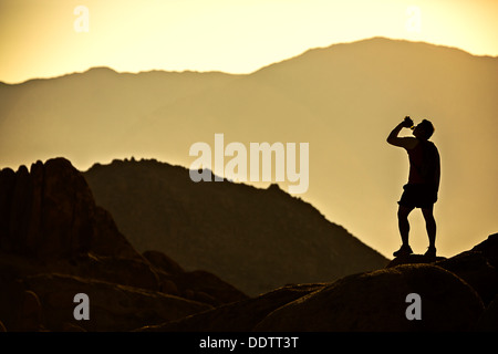 Ein einsamer Läufer in den Bergen für einen Drink aus seiner Wasserflasche hält an und wird von der Morgensonne Silhouette. Stockfoto