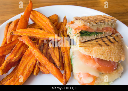 Geräucherter Lachs Panini Spinat Tomate Mozzarella Käse Pesto Mayo und Süßkartoffel Pommes frites Closeup Stockfoto