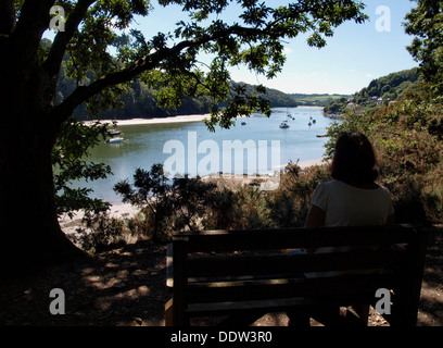 Frau saß auf einer öffentlichen Bank im Schatten eines Baumes in der Ansicht entlang dem Fluss Fal, Malpas, Truro, Cornwall, UK 2013 Stockfoto