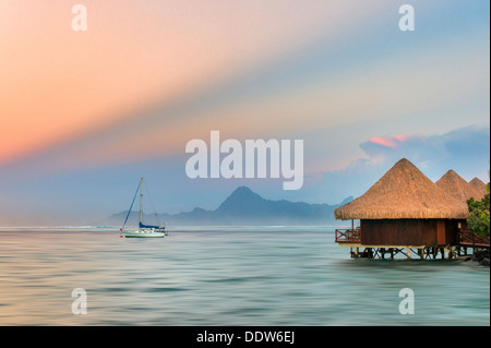 Die Bungalows über dem Wasser mit einem Segelboot und Sonnenaufgang und Moorea, Tahiti Stockfoto