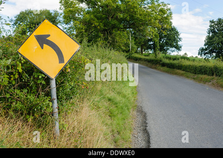 Gelbes Schild auf einer ländlichen Straße Warnung vor einer Linkskurve Stockfoto