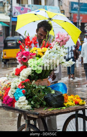 Indischer Mann Verkauf von Blumen aus einem Wagen im Regen. Puttaparthi, Andhra Pradesh, Indien Stockfoto