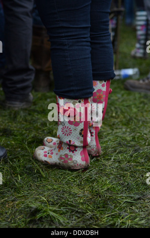 Person trägt bunt blühenden Wellington Stiefel stehen in einem nassen Feld auf einem Sommer-Musikfestival in England. Stockfoto