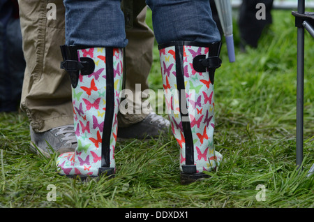 Person tragen bunte Schmetterling Wellington Stiefel stehen in einem nassen Feld auf einem Sommer-Musikfestival in England Stockfoto