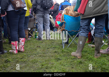 Menschen tragen Wellington boots stehen und sitzen in einem nassen Feld auf einem Sommer-Musikfestival in England Stockfoto