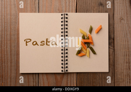 Eine Gruppe von bunten Pasta auf die leere Seite eines Notebooks. Der gegenüberliegende Seite hat das Wort, die, das Pasta ausgeschrieben. Stockfoto
