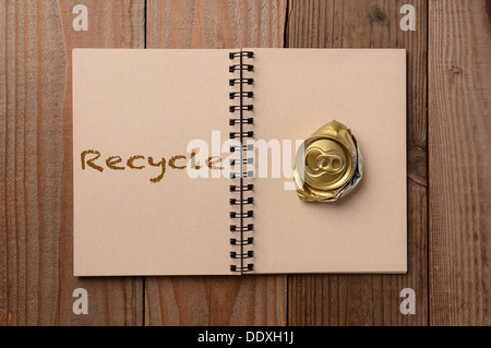 Eine zerdrückte Getränkedose auf der leeren Seite eines Notebooks. Der gegenüberliegende Seite hat das Wort, das Recycling ausgeschrieben. Stockfoto