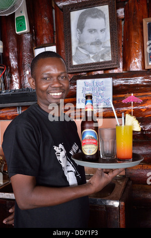 Kellner mit Kilimanjaro Bier und einen Cocktail vor einem Bild von Freddy Mercury, der späten Sänger der Rockband Queen, die Stockfoto