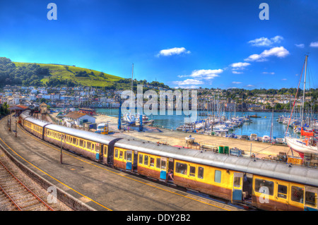 Zug am Bahnhof von Dartmouth Devon England mit gelben Wagen und die Stadt im Hintergrund mit blauer Himmel in HDR Stockfoto