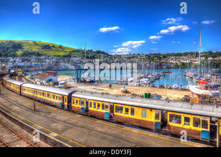 Dartmouth Bahnhof Devon England mit einem Zug mit gelben Wagen und die Stadt im Hintergrund mit blauer Himmel in HDR Stockfoto