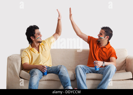 Glückliche junge männliche Freunde in Casuals geben ein High-Five zueinander Blechdosen mit gedrückter Stockfoto