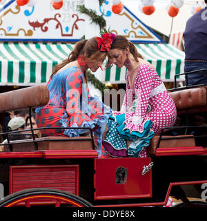 Zwei junge Frauen, die Flamenco-Kleider tragen, auf einem Schlitten auf der 'Feria de Abril' April Fair in Sevilla, Andalusien, Spanien, Europa Stockfoto