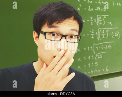 Junger Mann, asiatische, Studentin mit Brille, vor einer Tafel mit mathematischen Gleichungen, überrascht, verwirrt Stockfoto