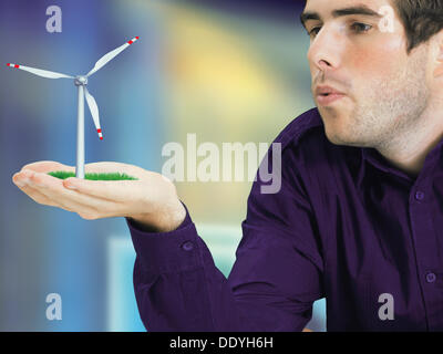 Mann bläst eine Miniatur-Windkraftanlage in der hand Stockfoto