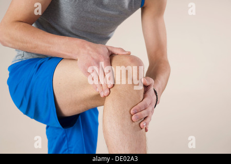 Junger Mann sein Knie untersuchen Stockfoto
