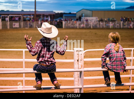 Junge & Mädchen gehockt Corral Zaun beobachten das Chaffee County Rodeo, Poncha Springs, Colorado, USA Stockfoto