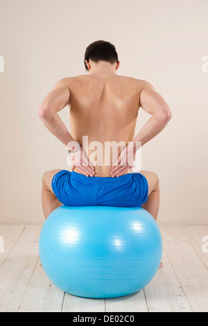 Junger Mann sitzt auf einem Gymnastikball und berührte seinen schmerzenden Rücken Stockfoto