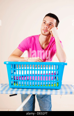 Junger Mann sucht verzweifelt und stützte sich auf ein Bügeleisen mit Bügelbrett Stockfoto