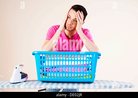 Junger Mann sucht verzweifelt und stützte sich auf ein Bügeleisen mit Bügelbrett Stockfoto