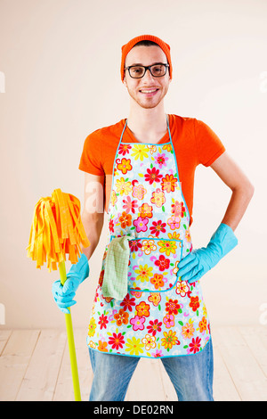Junger Mann trägt eine Schürze und Handschuhe halten Reinigung Mop Reinigung Stockfoto
