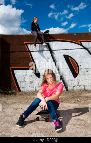 Zwei Mädchen im Teenageralter mit Skateboards vor einer Graffitiwand, Stadtgebiet Stockfoto