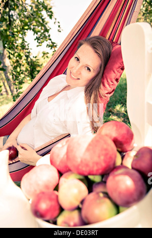 Schwangere Frau in Hängematte im Garten, Äpfel vor Stockfoto