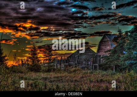 Alten Wirtschaftsgebäude bei Sonnenaufgang. Schöne Farben von orange dramatische Wolken und blauer Himmel und grünen Bäumen. Schöne Landschaft Stockfoto