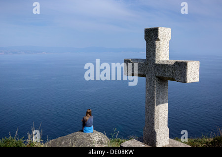 Ein Tourist sitzt auf den Klippen nahe des Leuchtturms von Finisterre, das Ende ein Stück des Jakobswegs. Stockfoto