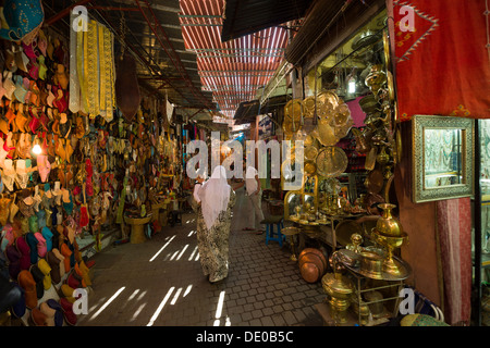 Marokkanische Frau in traditioneller Kleidung, die von einem Ladenbesitzer angesprochen, wie geht sie durch einen Souk in Marrakesch, Marokko Stockfoto