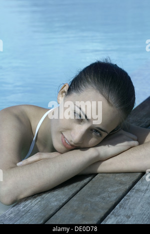 Frau im Pool an Deck, gelehnt auf Arme Kopf ruht Stockfoto