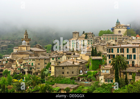 Dorf mit Regenwolken, hinter dem Kartäuser-Kloster, im Vordergrund die Pfarrei Kirche Sant Bartomeu, Valldemossa, Region anzeigen Stockfoto