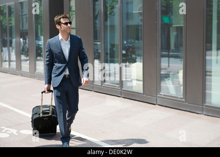 Geschäftsmann mit Sonnenbrille ziehen Gepäck, zu Fuß in die Stadt Stockfoto