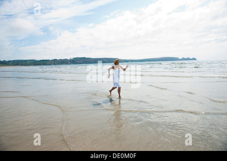 Frau rennt durch kleine Wellen am Strand Stockfoto