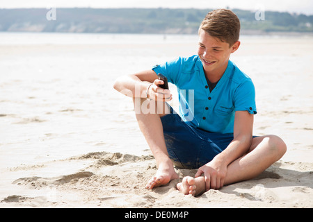 Teenager mit seinem Smartphone am Strand Stockfoto