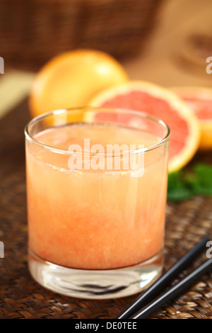 Frisch gepressten Saft der Grapefruit rosa prall mit schwarzen Trinkhalme auf der Seite und Grapefruits in den Rücken Stockfoto