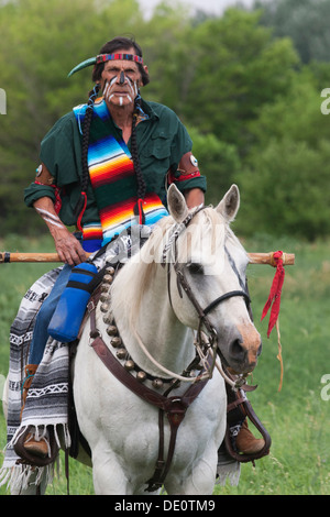 Krieger in Comanche Kleidung und Kriegsfarbe Reiten auf weißem Pferd Stockfoto