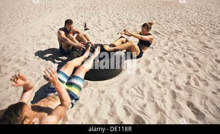 Drei junge Athleten Bauch-Übung mit einem LKW-Reifen am Strand zu tun. Athleten, die Crossfit Training im Freien zu tun Stockfoto